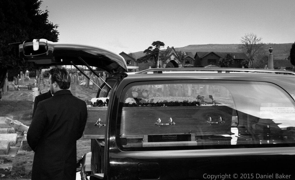 black and white photo of a funeral casket being lifted out of the back of a hearse