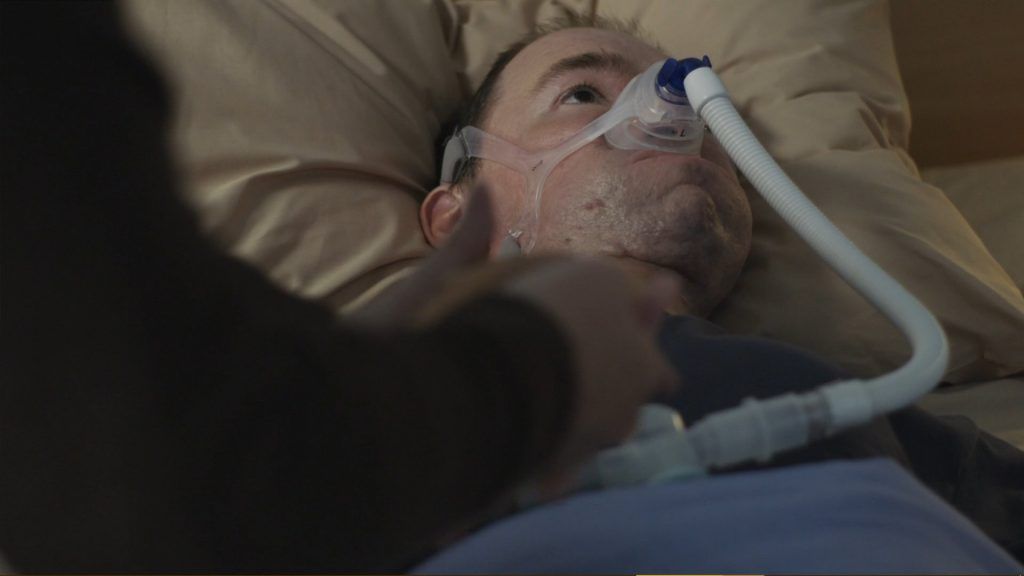 Daniel Baker laying in a bed with Brendan Coyle holding his hand copyright 2018 BBC One