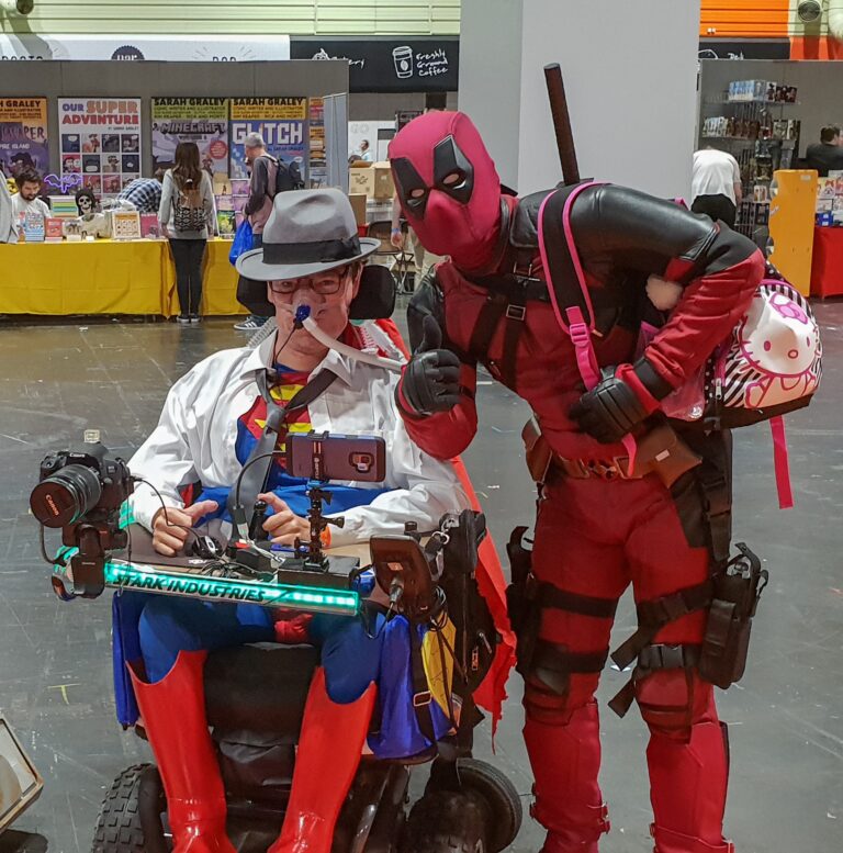 Daniel Baker in his wheelchair dressed as Clark Kent/Superman with Deadpool beside him