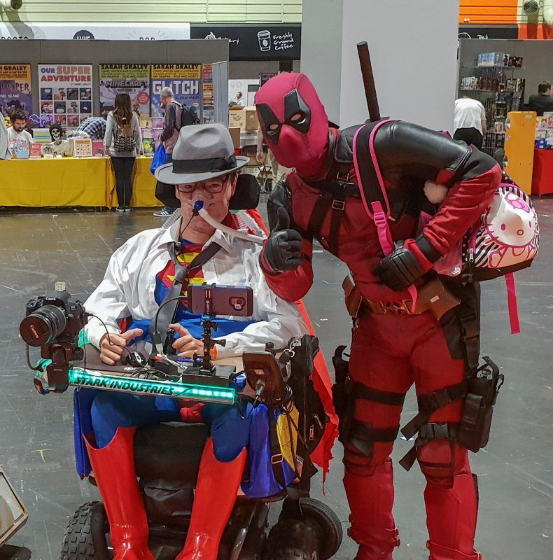 Daniel Baker in his wheelchair dressed as Clark Kent/Superman with Deadpool beside him