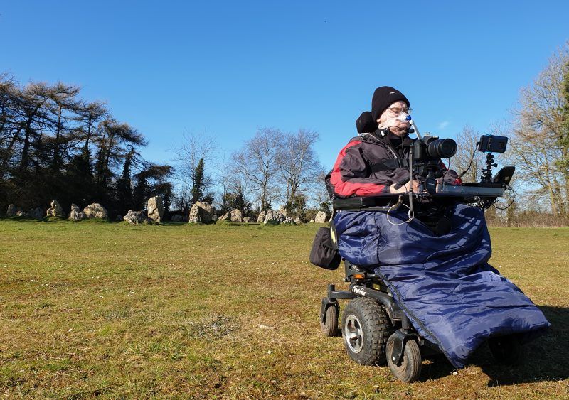 Daniel Baker in his wheelchair sitting in front of a neolithic stone circle 