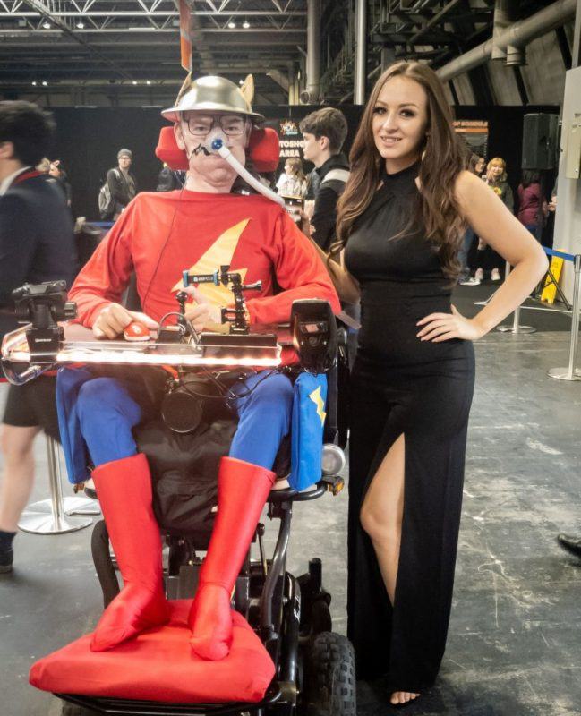 Daniel Baker in his wheelchair dressed as Jay Garrick with Tabitha Lyons in a long black dress standing beside him at Mcm Commiccon Birmingham 2019