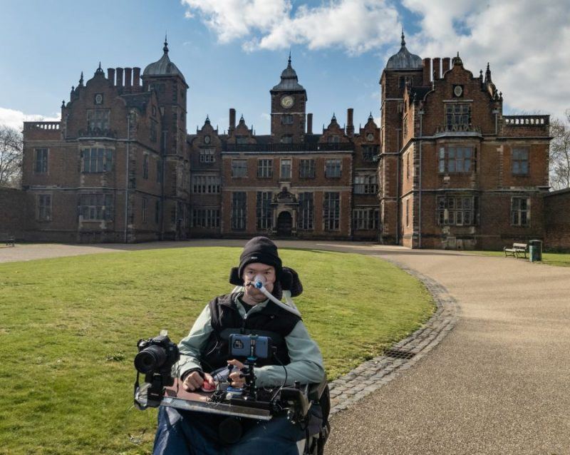 Daniel Baker in his wheelchair sitting in front of Aston Hall
