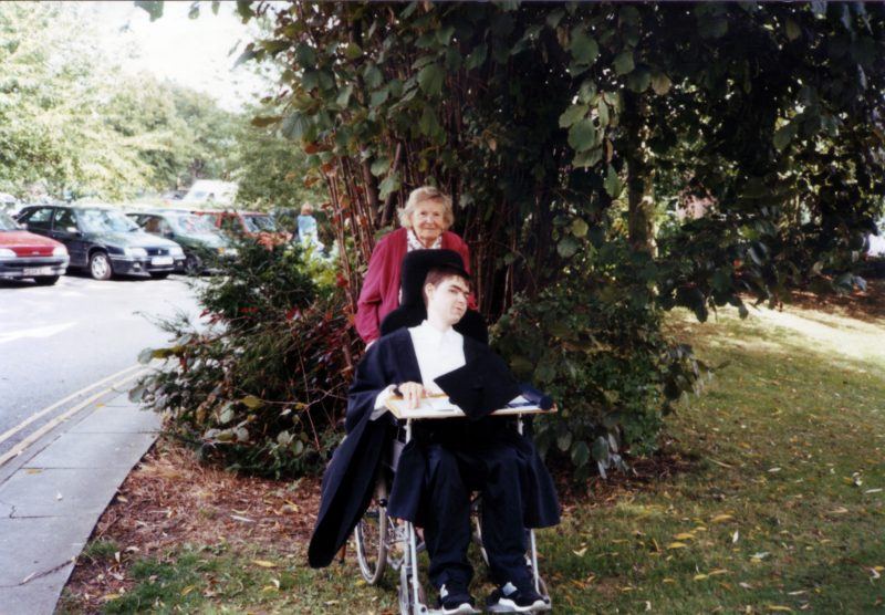 Daniel Baker in his graduation gown sitting outside Oxford Brookes University with his Nan Olive Baker standing behind him