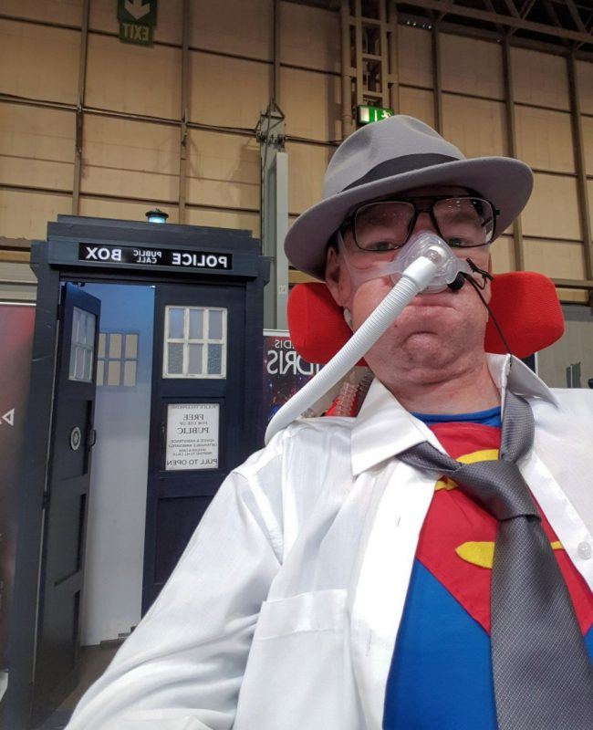 Daniel Baker at Collectormania 26 wearing a Superman/Clark Kent cosplay in front of a TARDIS