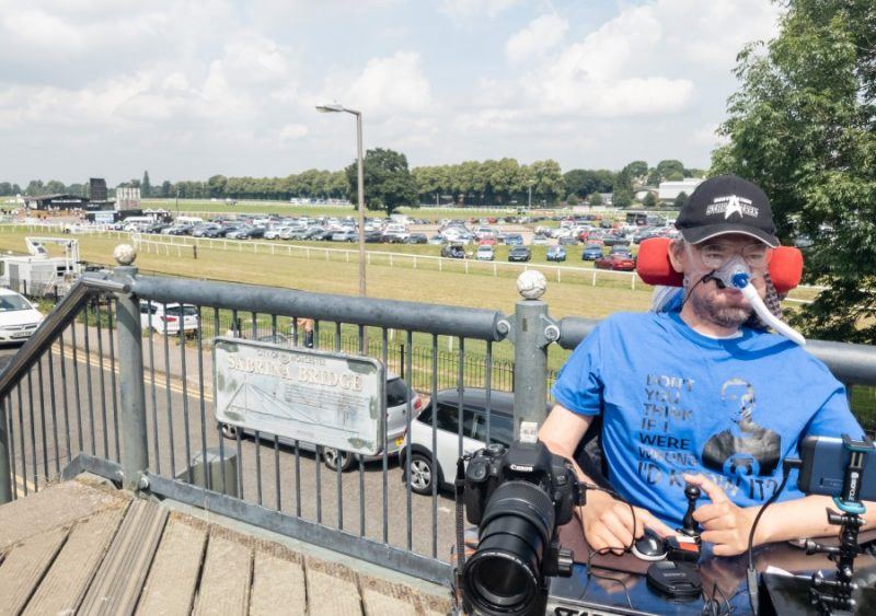 Daniel Baker sitting on a bridge overlooking Worcester raceecourse, wearing a blue big bang theory t-shirt which reads " Don't you think if I was wrong I'd know it?"