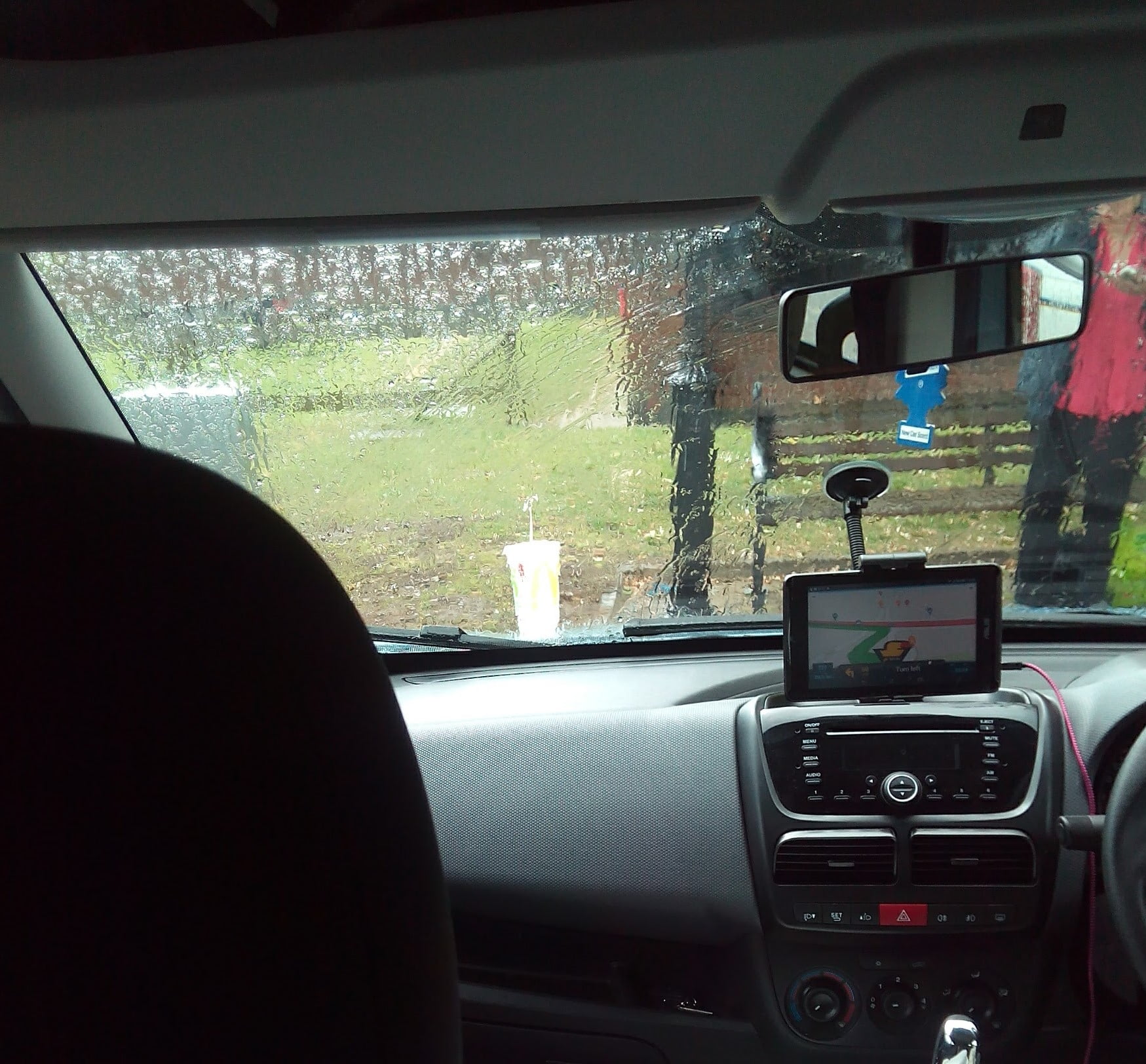 View from inside a van with rain on the windscreen and a woman barely visible dialling a number on her mobile phone 