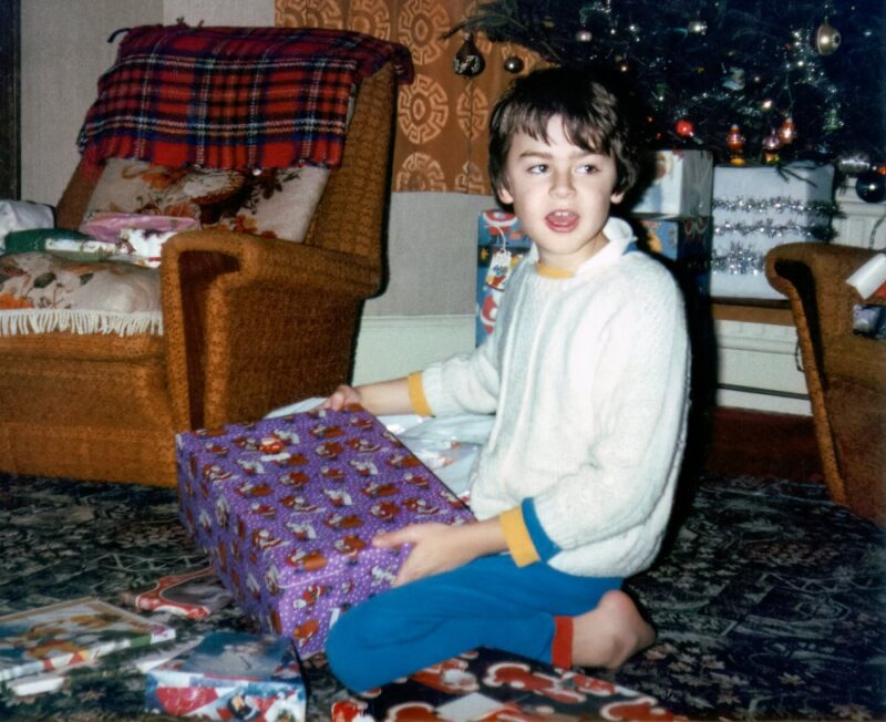 an old photo of a child opening Christmas presents.