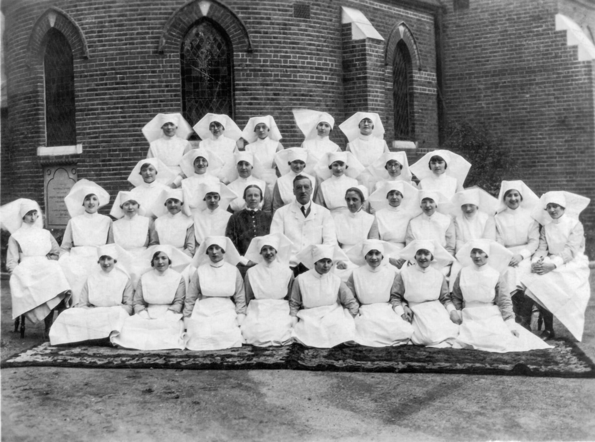 Black and white photo of a class of nurses posing for a photo outside a large brick building