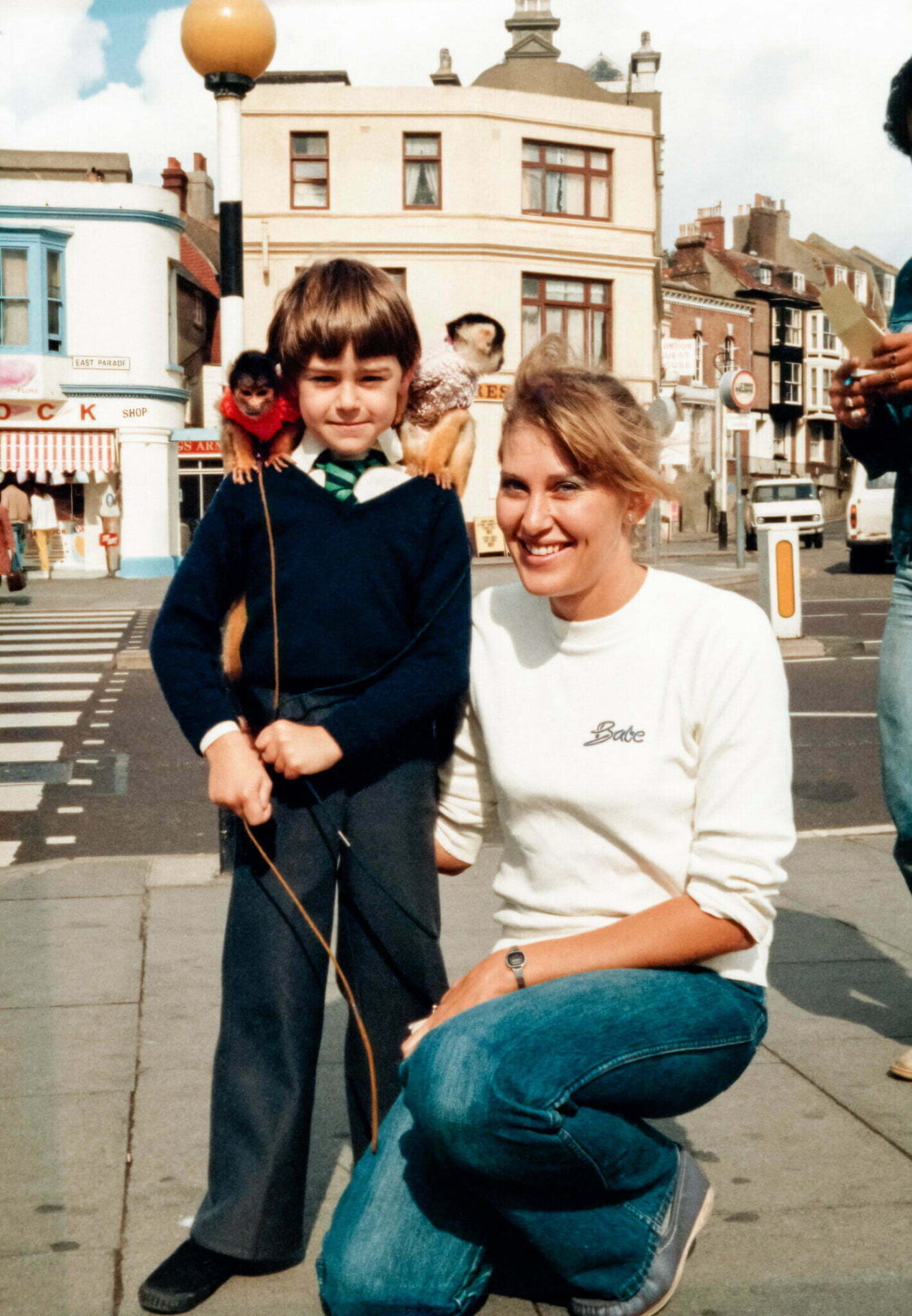 a woman kneeling down next to a boy with monkeys sitting on his shoulders at the seaside.  (Daniel Baker and his Mother)