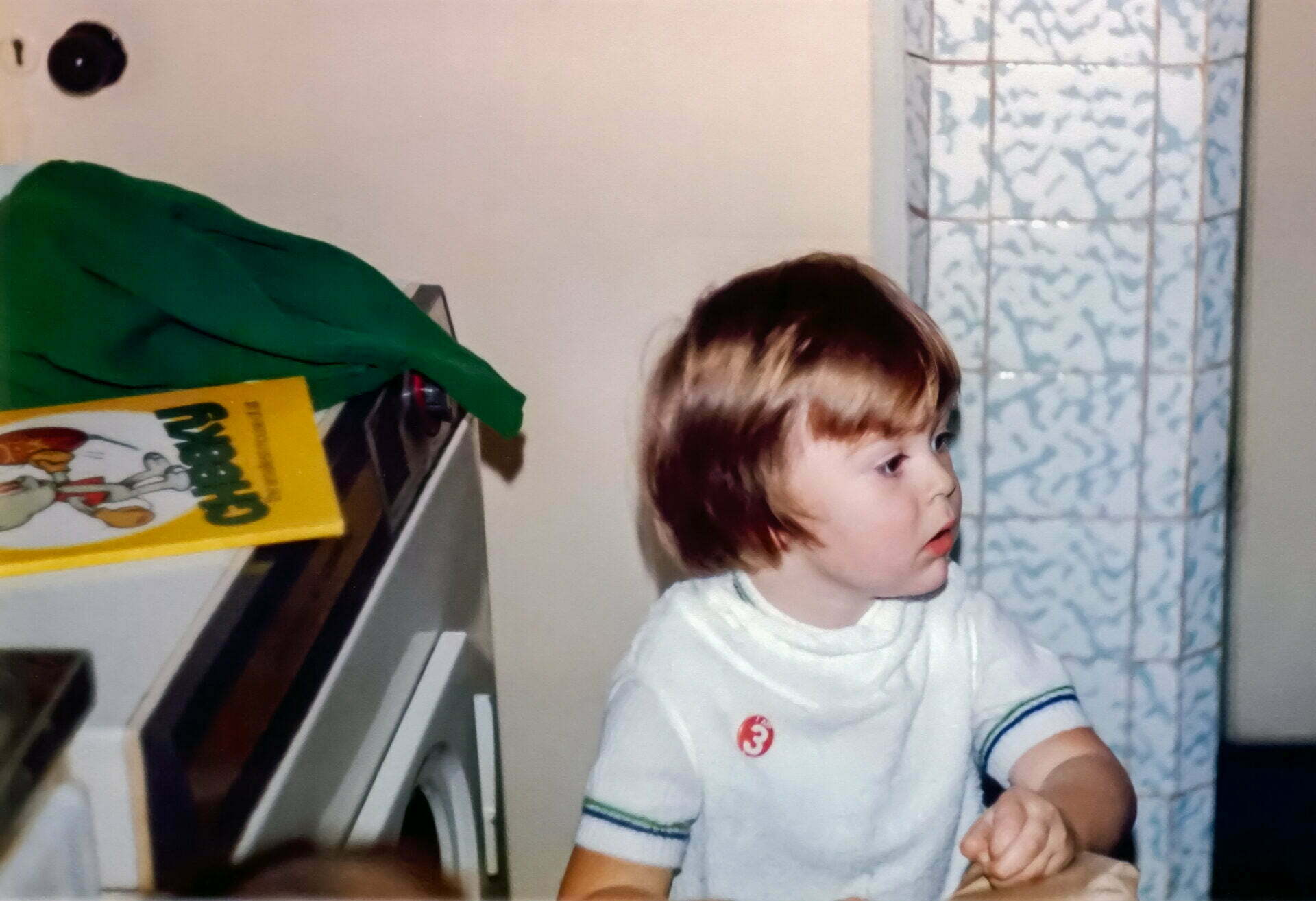 A young boy in a t-shirt wearing a red I am 3 badge
