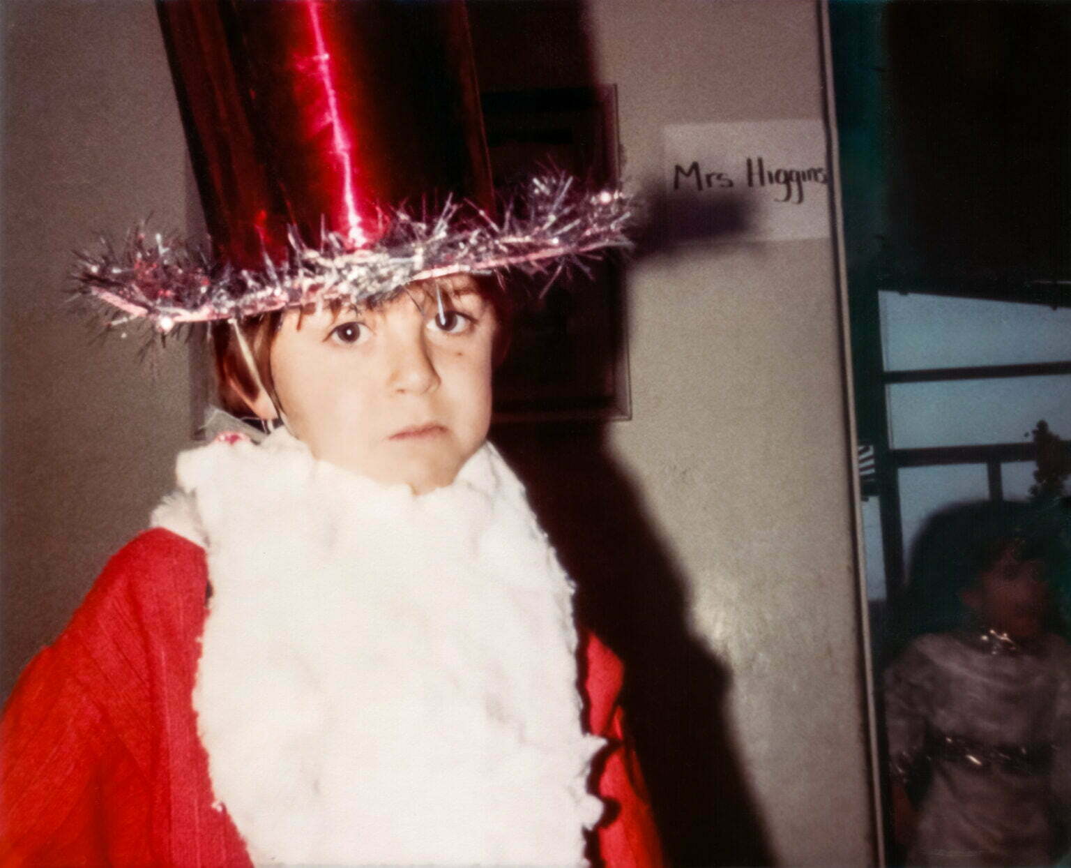 a young boy dressed as Father Christmas for a school play wearing a tinsel hat and a red suit.