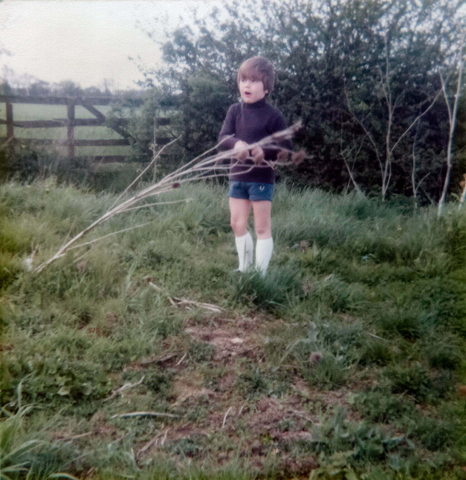 A young Daniel Baker standing in a field holding a stick