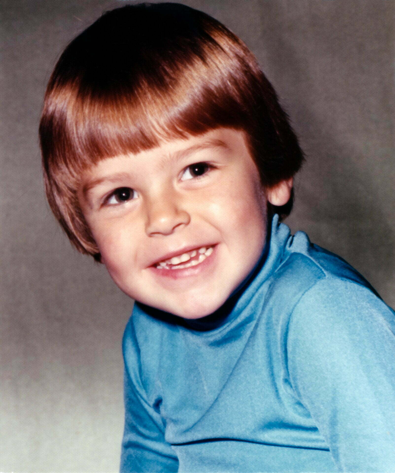 a young boy is smiling for a picture wearing a blue sweater.