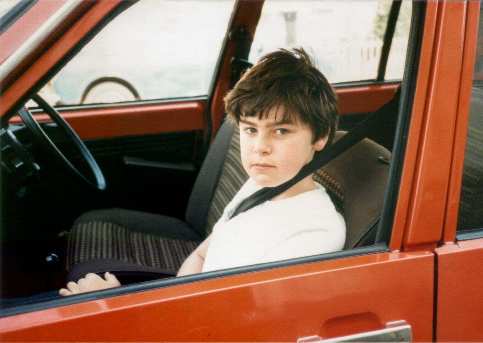 a young boy sitting in a red car.