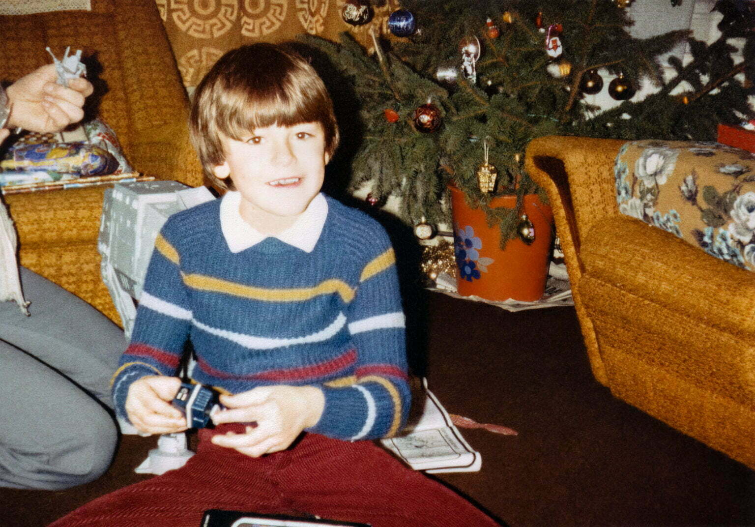 a young boy sitting on the floor next to a christmas tree playing with a robot.