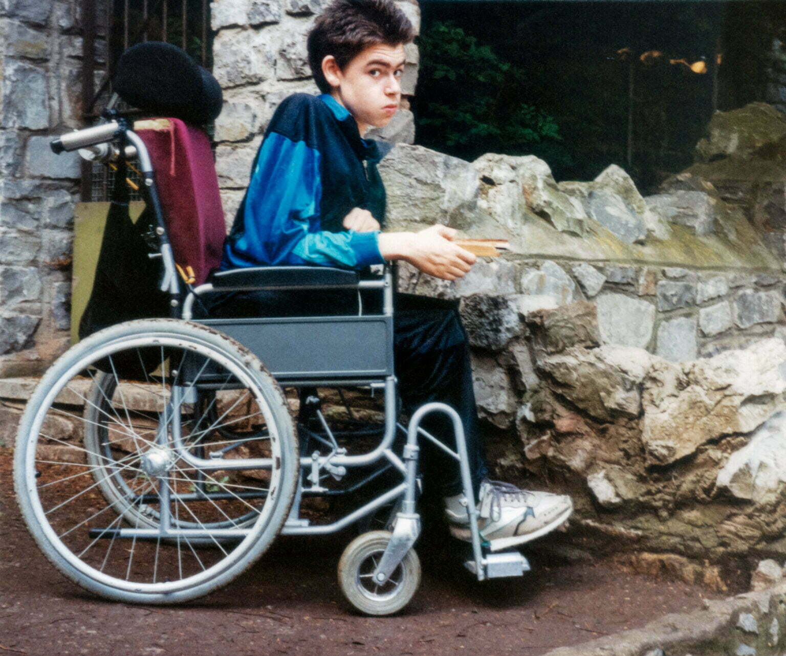 Daniel Baker sitting in a wheelchair next to a stone wall.