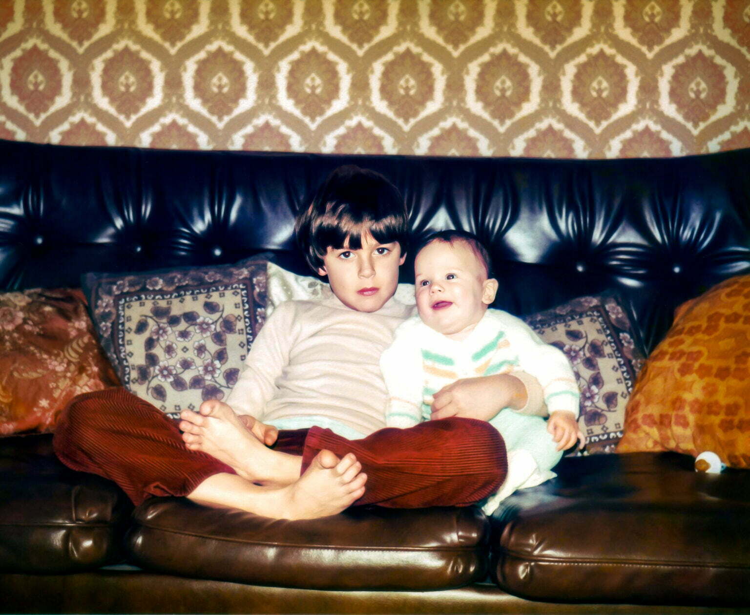 A young Daniel Baker sitting on a leather sofa next to his baby cousin Martin