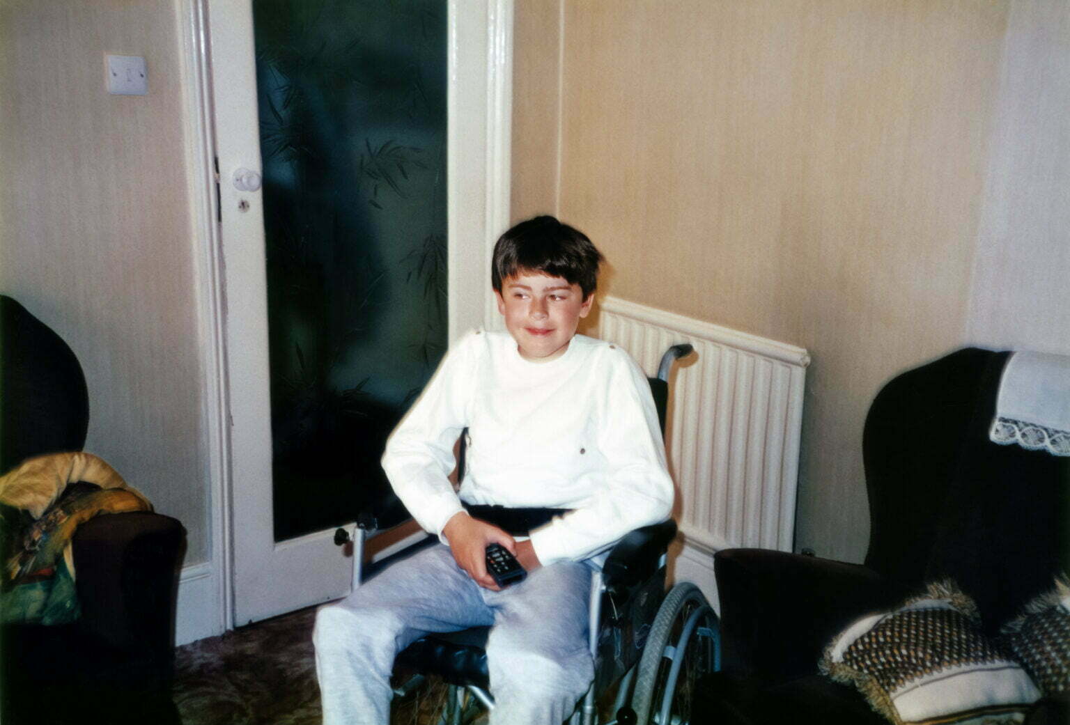 A young Daniel Baker sitting in a wheelchair in a living room