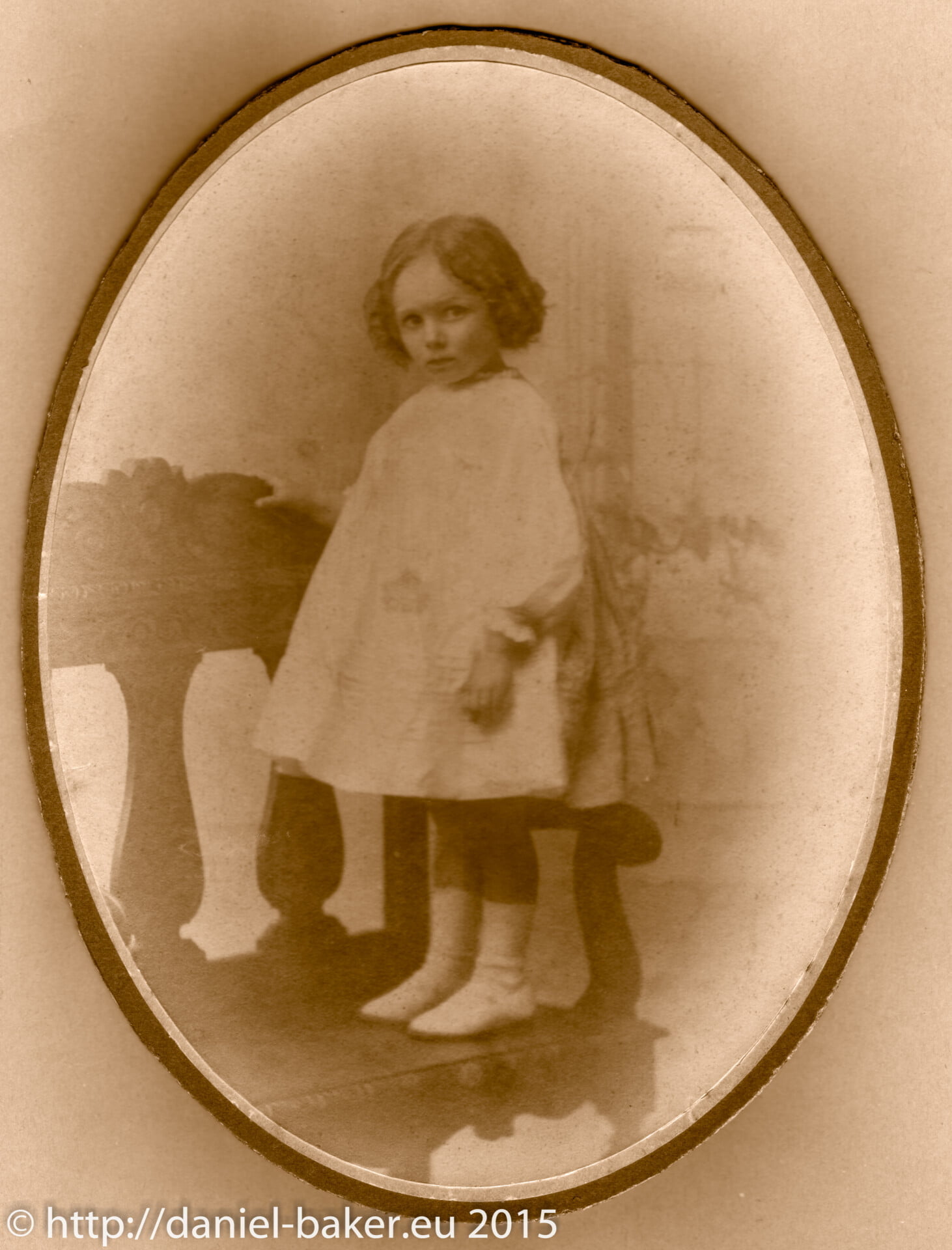 A sepia photograph of a young girl standing on a sofa wearing Victorian style clothes