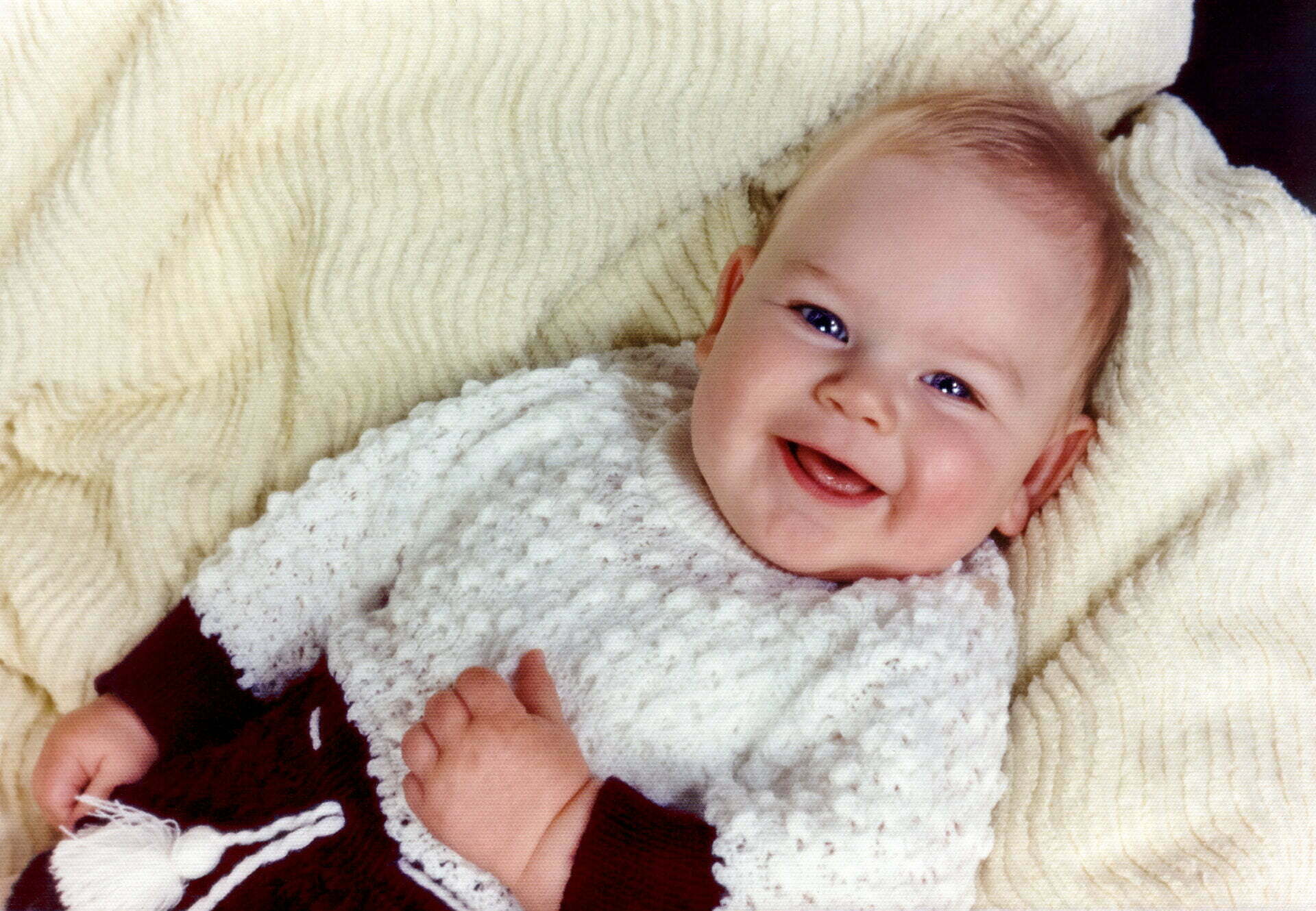 a baby smiles while laying on a blanket.