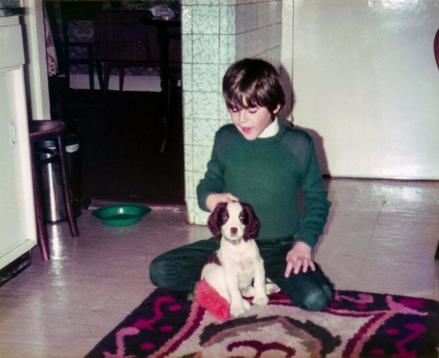 Daniel Baker sitting cross legged on a rug in a kitchen stroking a cocker spaniel puppy named Atari