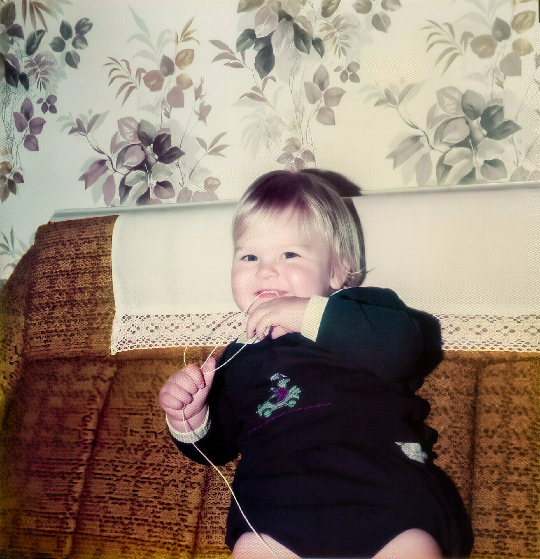 A very young Daniel Baker sitting on a sofa playing with a piece of string