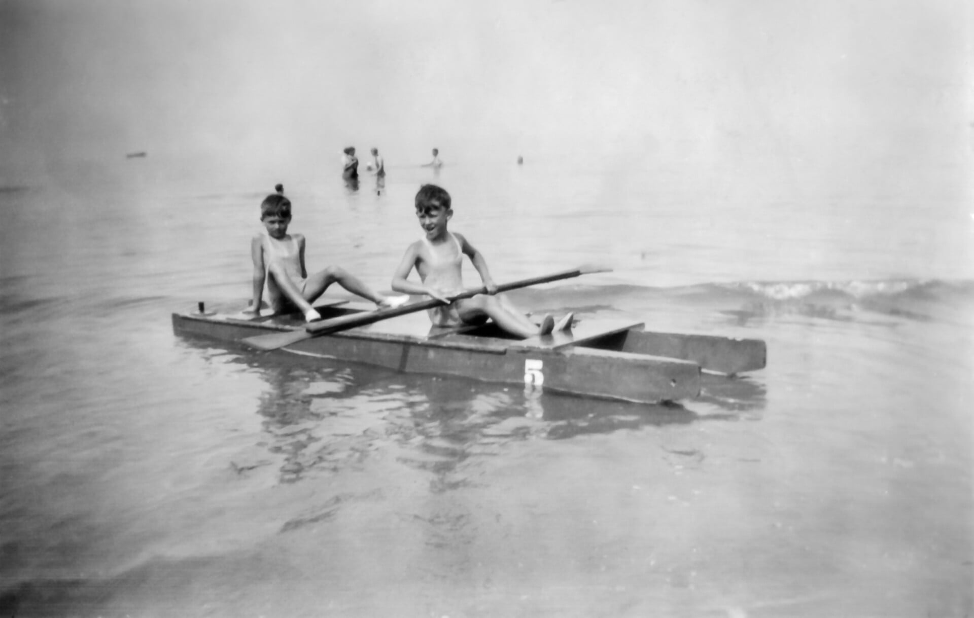 Black and white photo of two children rowing a boat in the sea