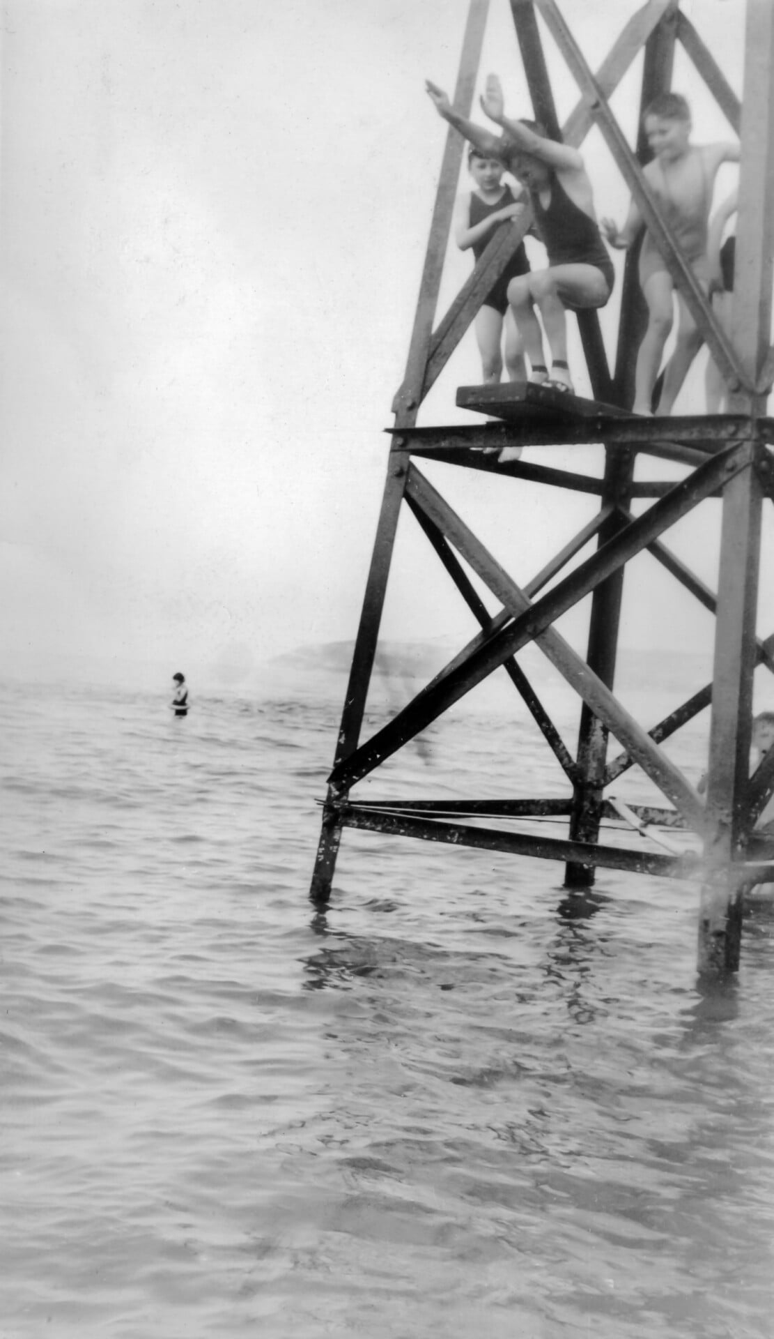 Black and white photo of three children on a wooden tower in the sea