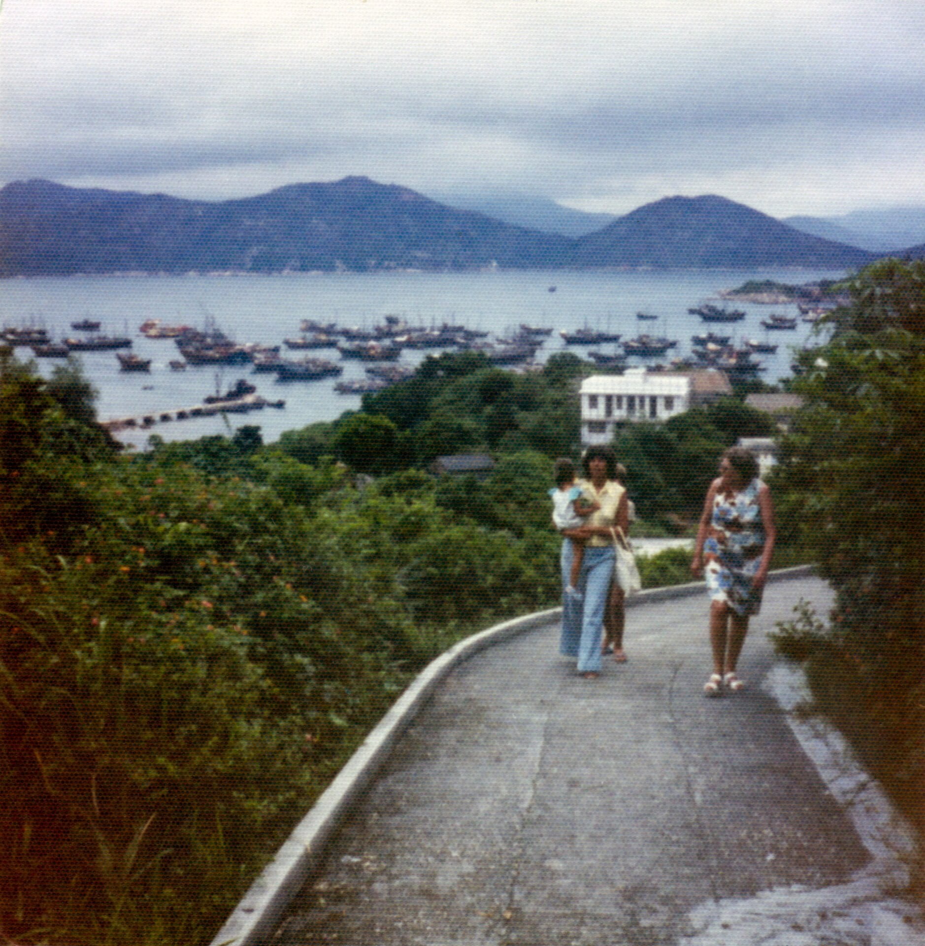 Two women walking up a steep slope with two children, a bay in the distance below