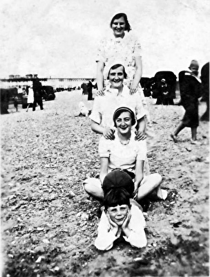 black and white photo of four people one behind the other facing the camera on a beach
